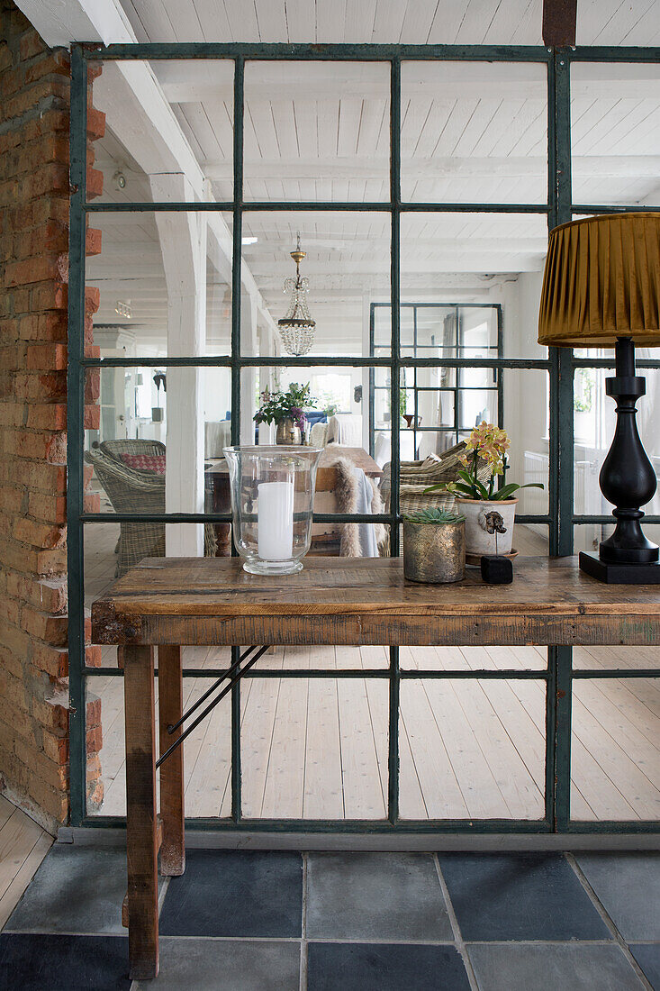 Folding table with lantern, flowering plant and lamp in front of large industrial window