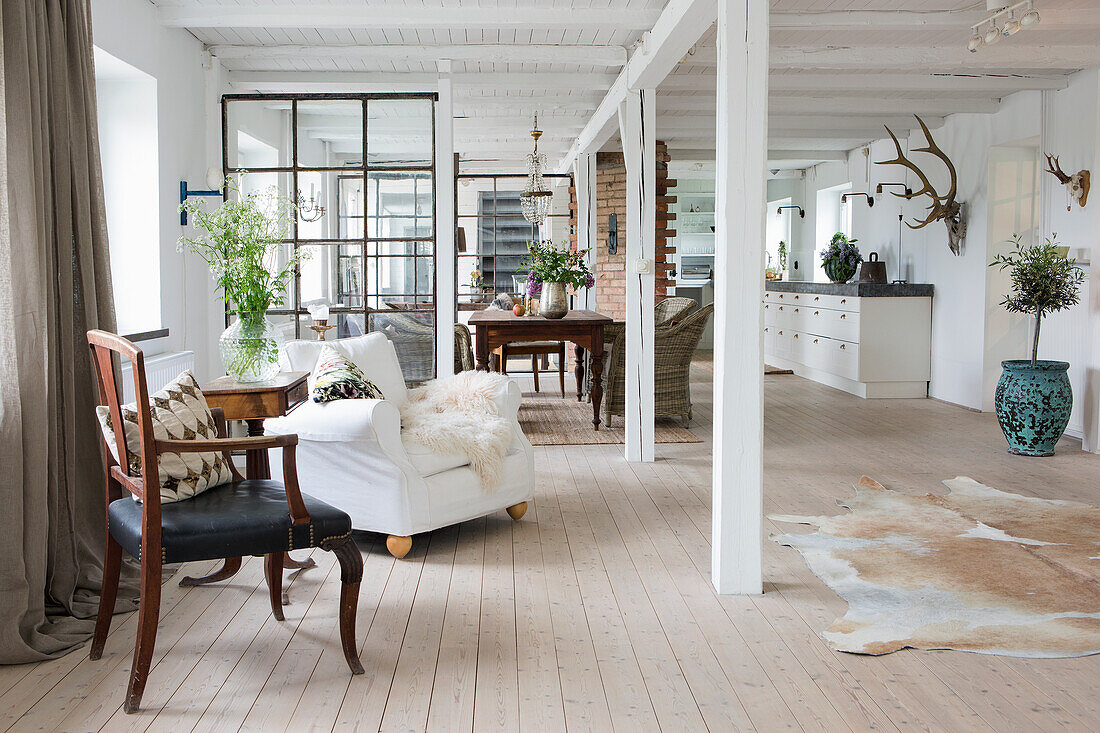Sitting area in light, open-plan interior with white-painted wooden beams
