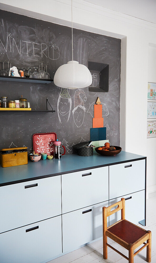 Light-colored kitchen cabinets, above it is a chalk board wall with drawings