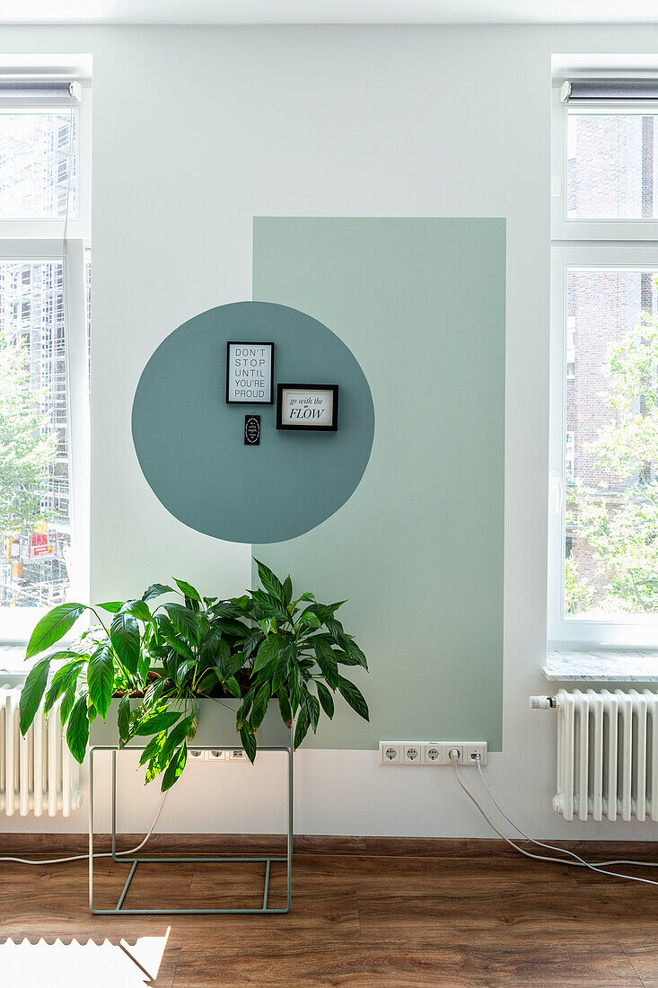 Helle Wand mit grünen, geometrischen Akzenten, davor Pflanzenständer im Büro