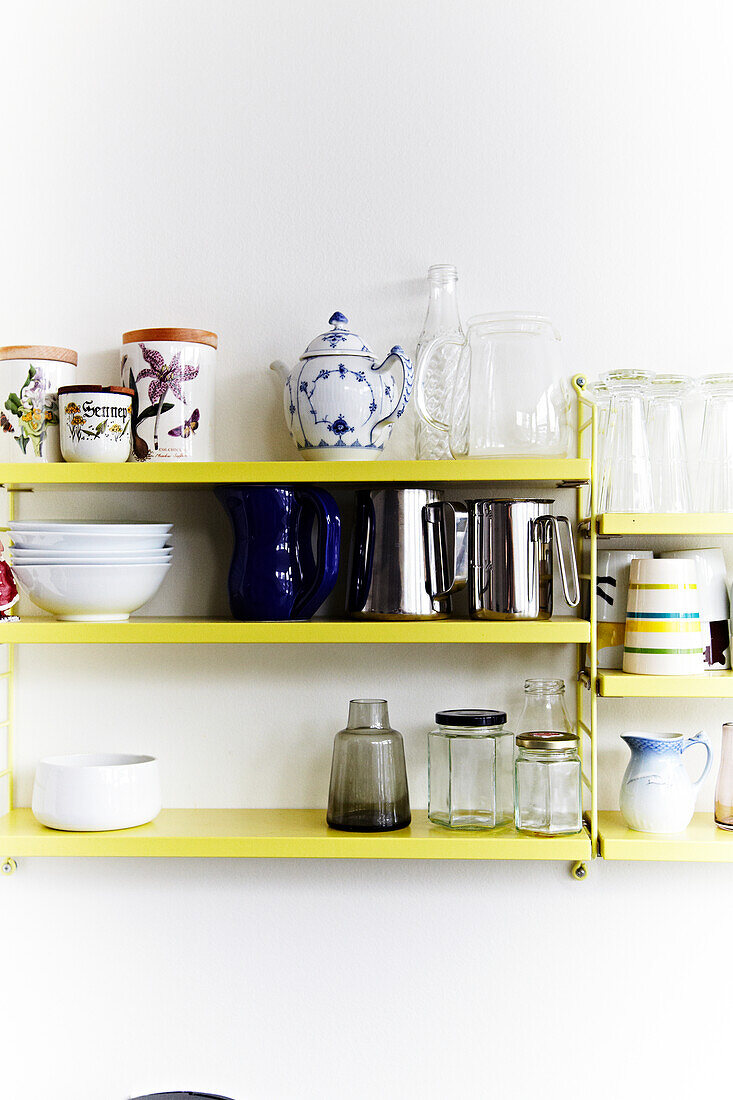 Yellow wall shelf with crockery, storage jars, jugs and glasses