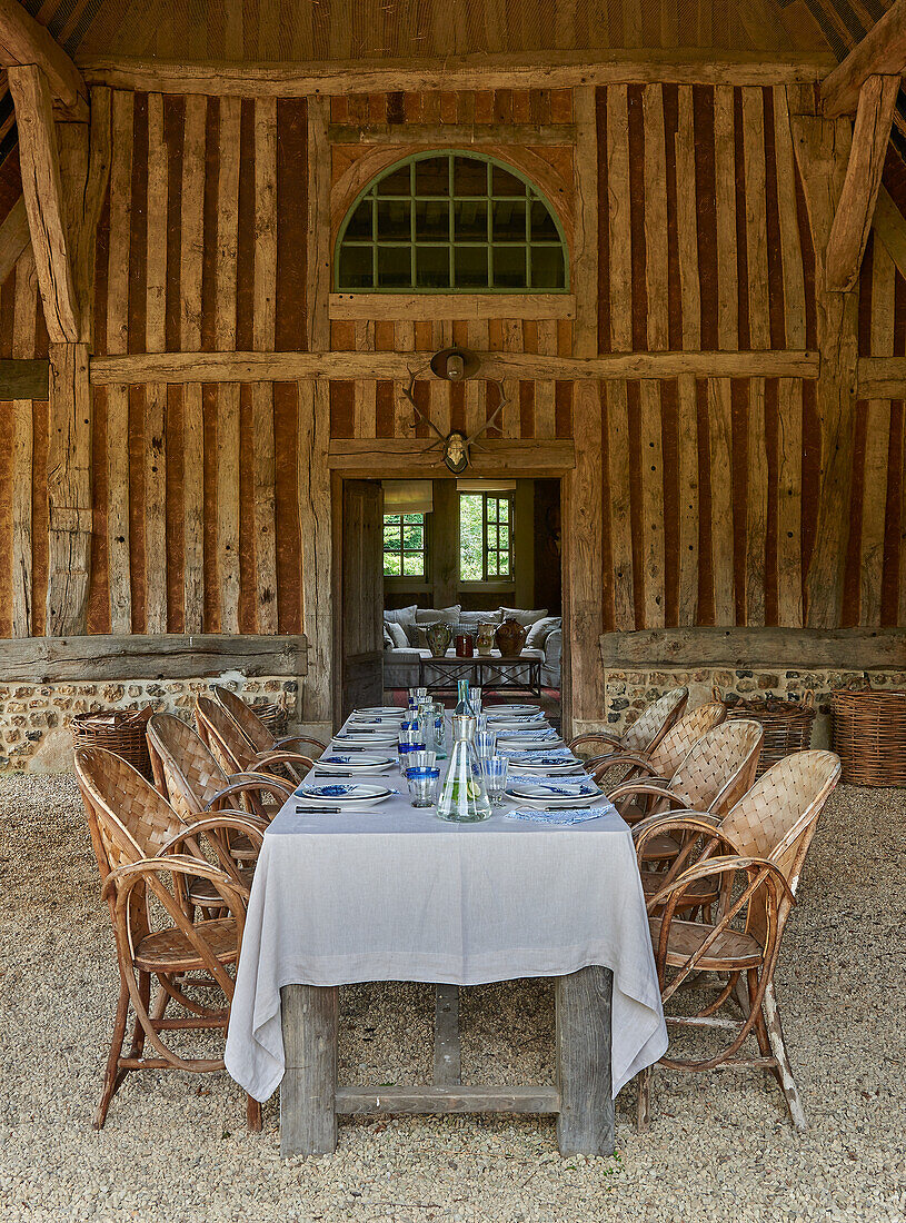 Langer, gedeckter Tisch mit Rattanstühlen vor französischem Landhaus