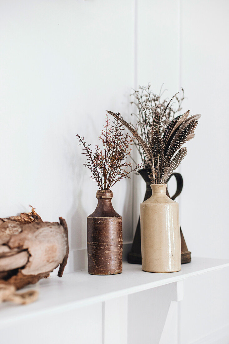 Clay vases with feathers and twigs as rustic boho decoration on a shelf