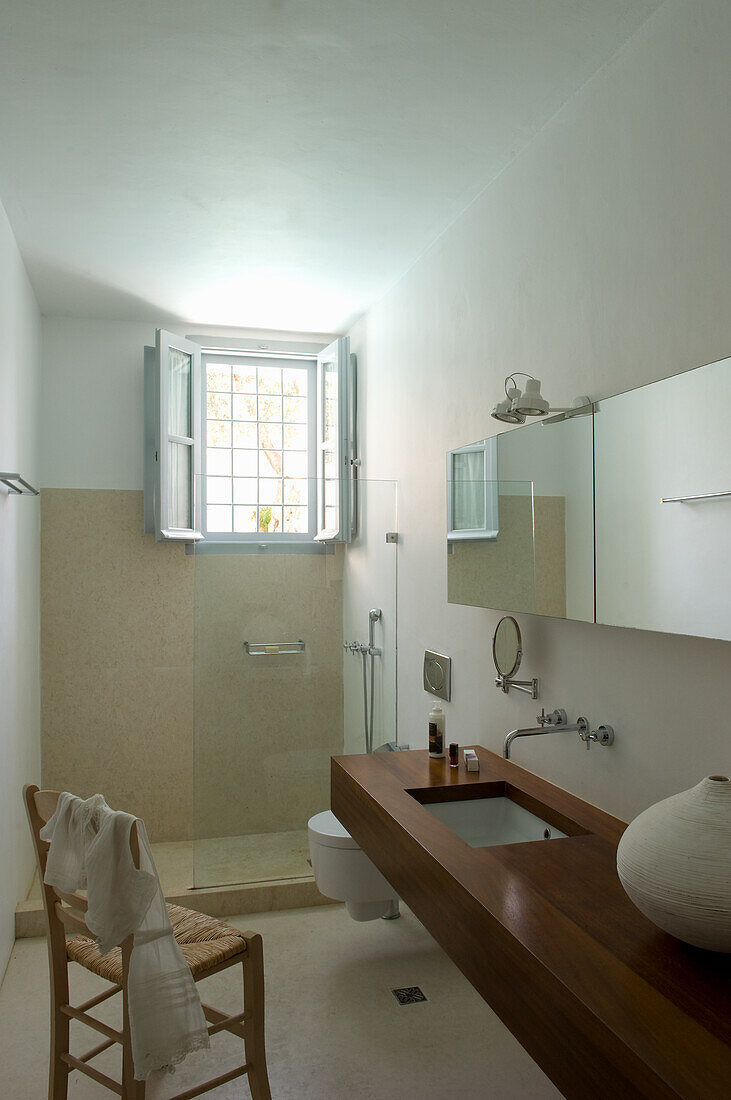 Long wooden bathroom counter with a sink, chair, toilet and shower area