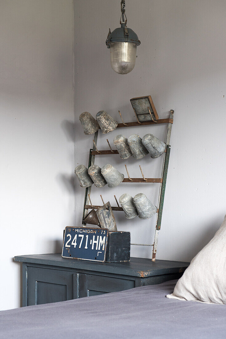 Enamelled vessels on battered rack on top of old blue cupboard used as bedside table in bedroom