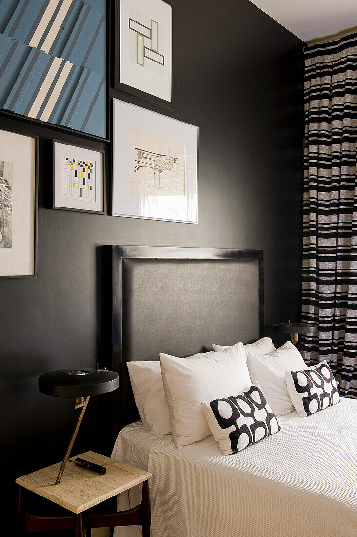 Doppelbett, darüber moderne Bilder im Schlafzimmer mit schwarzer Wand