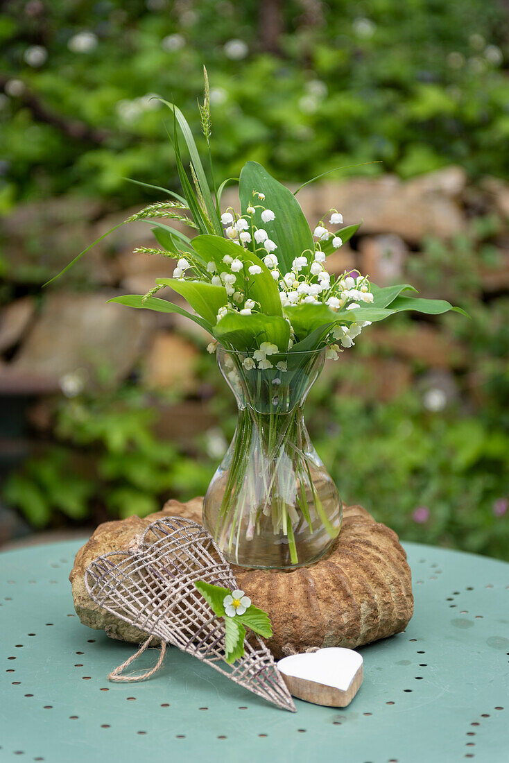 Small bouquet of lily of the valley and heart decoration on garden table (Convallaria majalis)