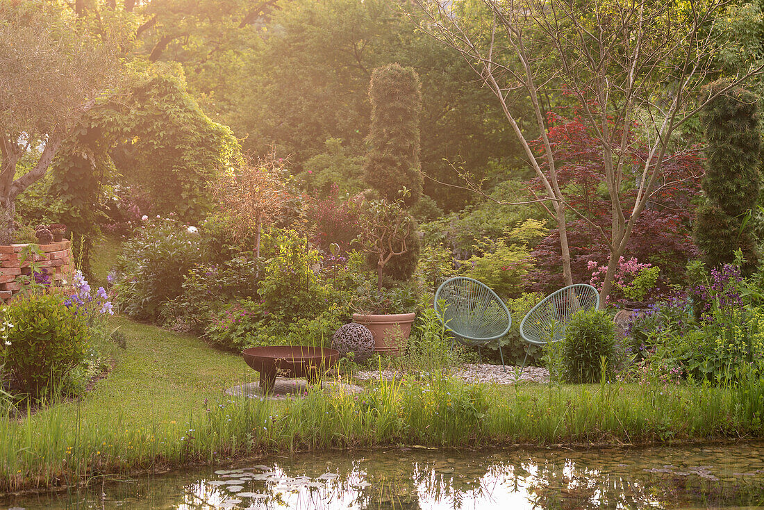 Blick über Teich auf Sitzplatz in üppig bewachsenem Garten