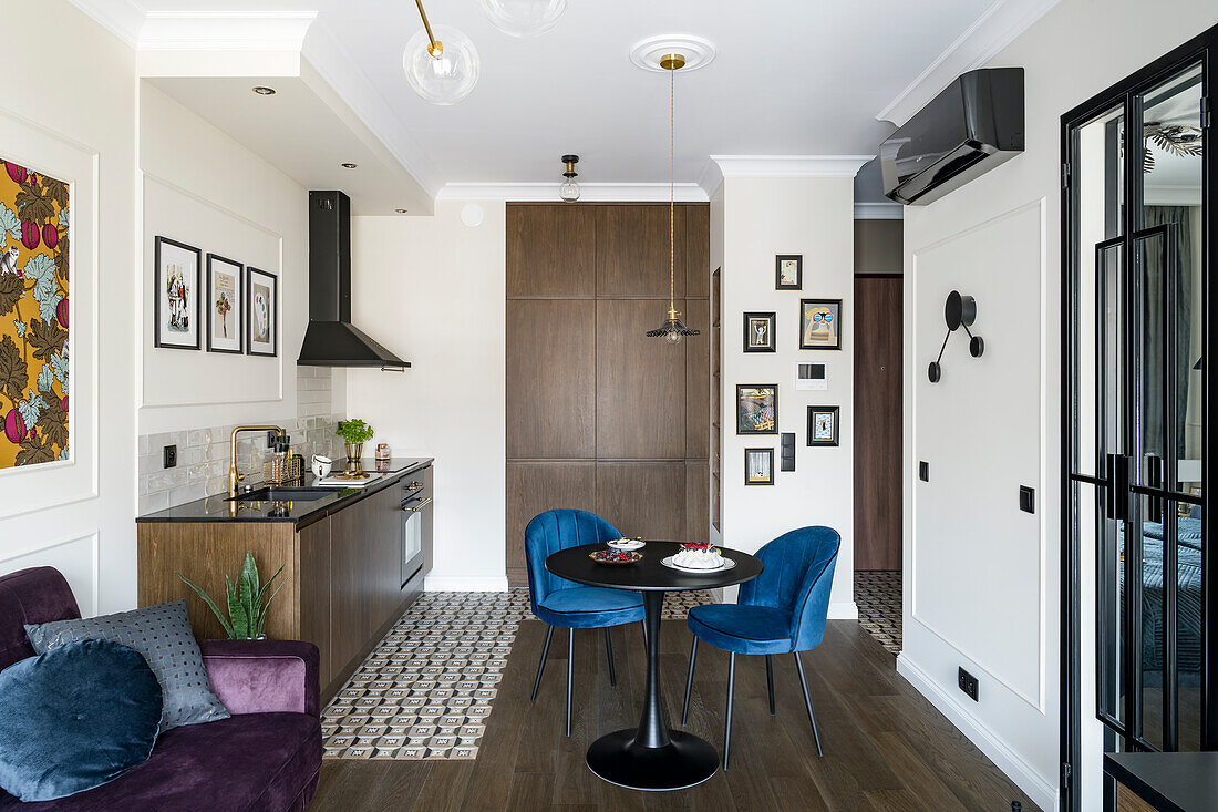 Essbereich mit blauen Polsterstühlen vor kleiner Küchenzeile und lila Sofa in offenem Wohnraum