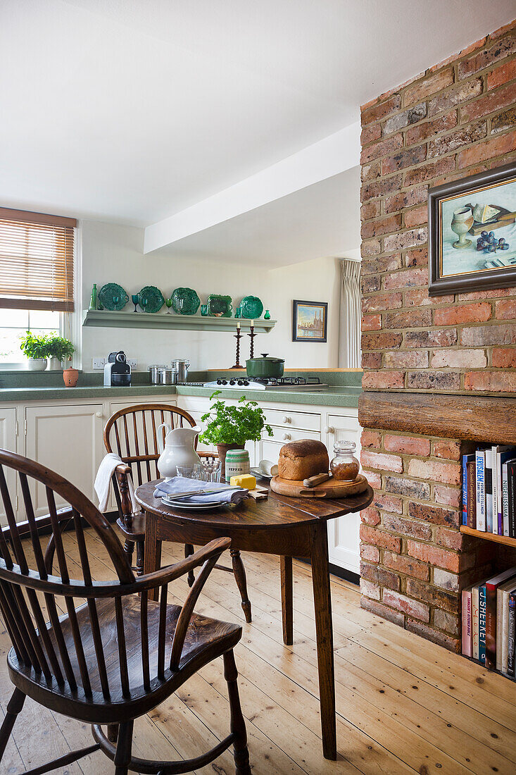 Small round table with wooden chairs in front of brick wall in open-plan kitchen