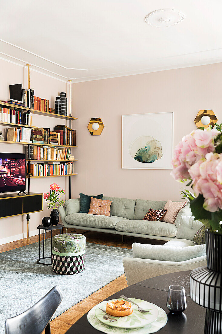 Wohnzimmer mit Regalwand, Polstersofa und rosa Wand, im Vordergrund Esstisch