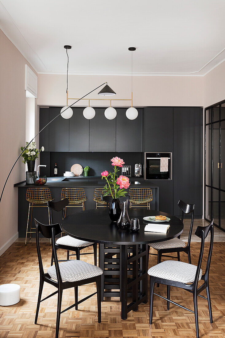 Elegante schwarze Küche mit Theke, im Vordergrund runder Tisch mit Stühlen