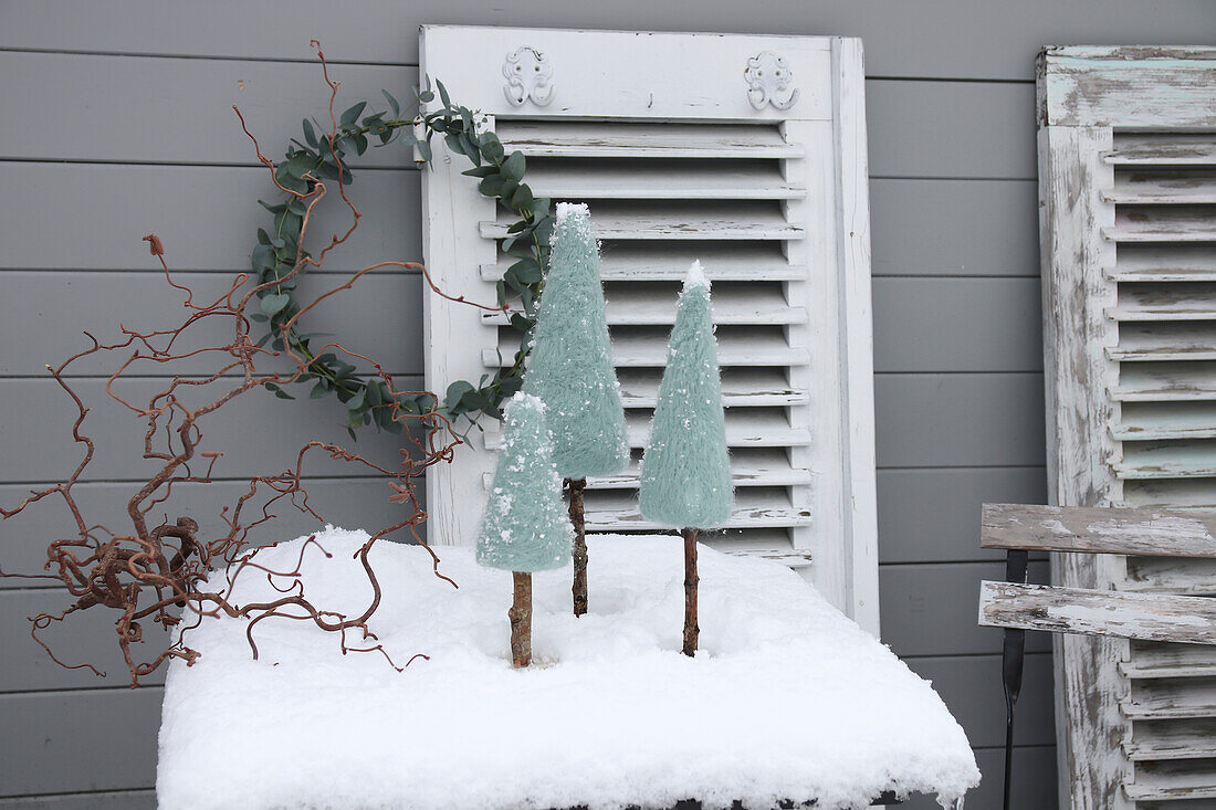 Winterliche Dekoration mit schneebedeckten Tannenbäumen aus Holz auf Tisch