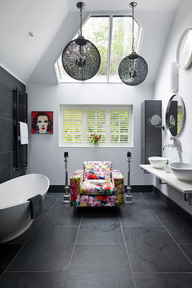 Armchair with floral upholstery in bathroom with white walls and black slate tiles
