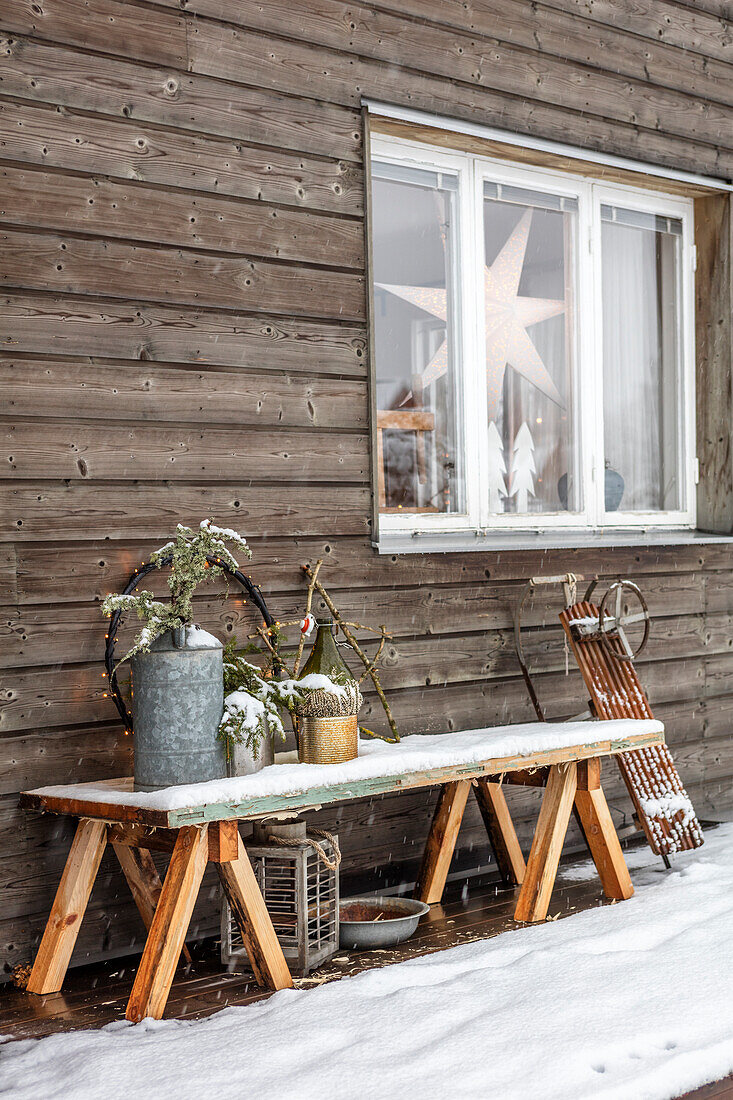 Winterliche Deko auf Bank vor Holzhaus und Schlitten an Holzwand