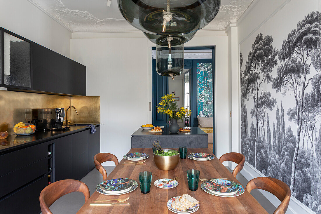 Kitchen with dining table, black cabinets and wallpaper with trees