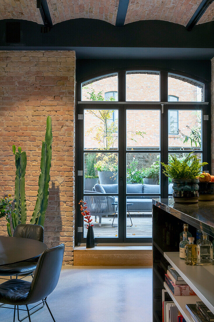 Loft-Wohnzimmer mit Kaktus neben Fensterfront und Terrassenzugang