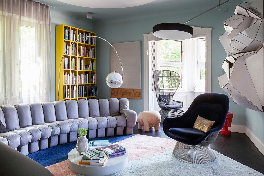 Wohnzimmer mit halbrundem Sofa, Teppich, Bücherregal und Bogenlampe