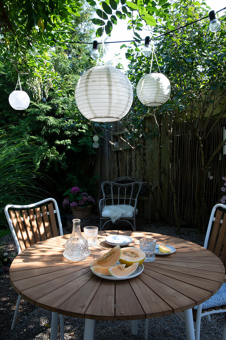 Round patio table with chairs, lanterns above in the garden