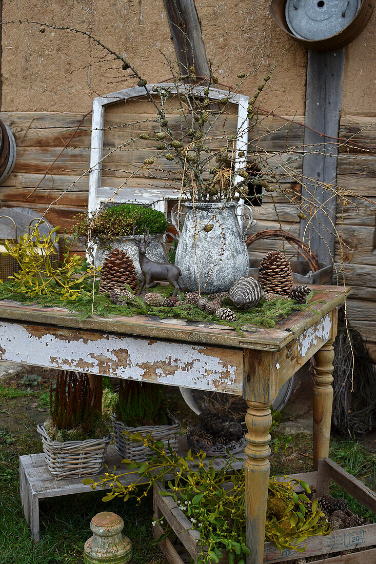 Alter Tisch mit Steintöpfen, Lärchenzweigen und Zapfen im Garten