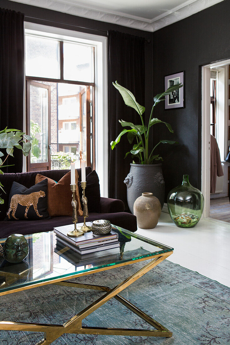 Living room with dark walls and dark sofa, indoor plants and glass table