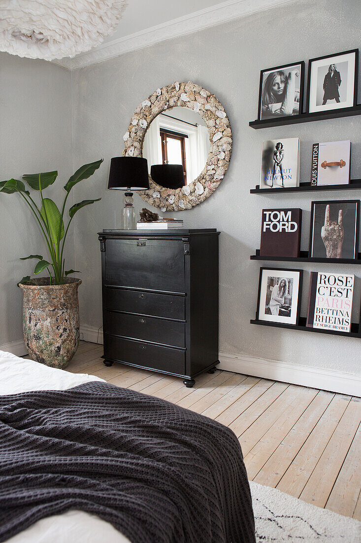 Schlafzimmer mit schwarzer Kommode, Wandregalen, rundem Spiegel und Pflanzendekoration