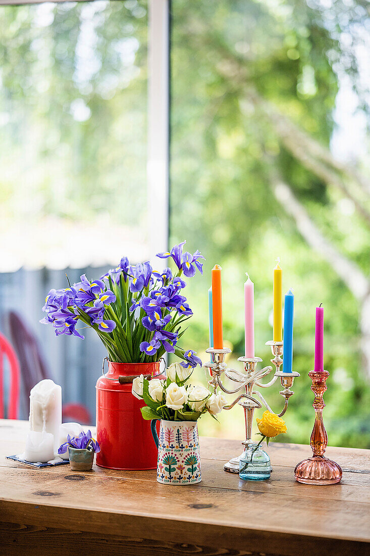 Holztisch mit Schwertlilien, weißen Rosen und bunte Kerzen