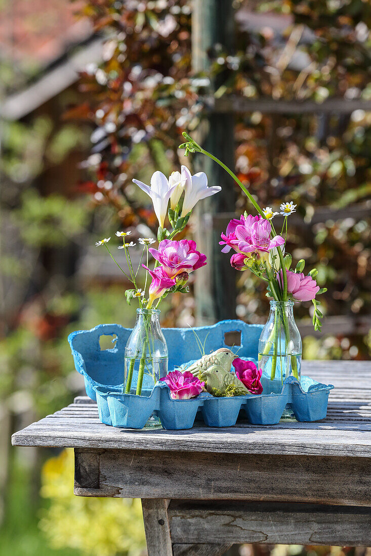 Sträußchen aus Freesien und Kamillenblüten in Glasvasen, Vogelfiguren und blauer Eierkarton
