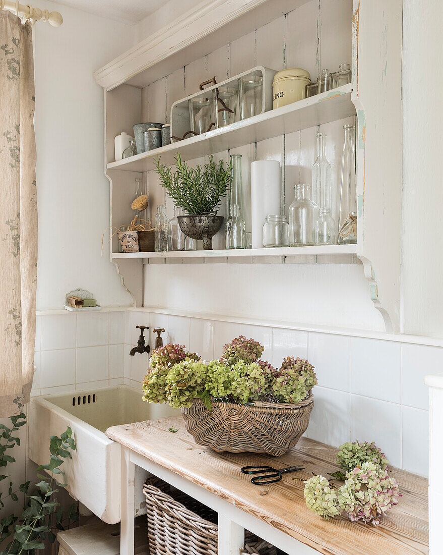 White vintage kitchen shelf with crockery and hydrangeas in a basket