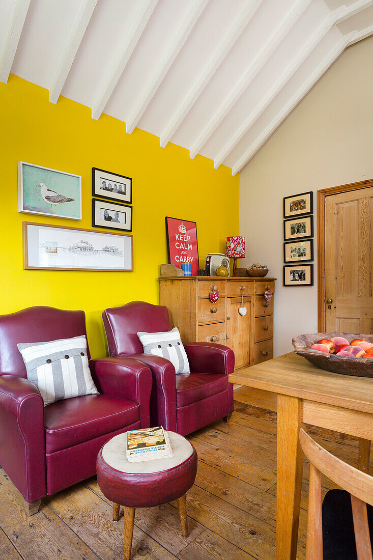 Dining area with yellow wall, red leather armchairs and leather stools