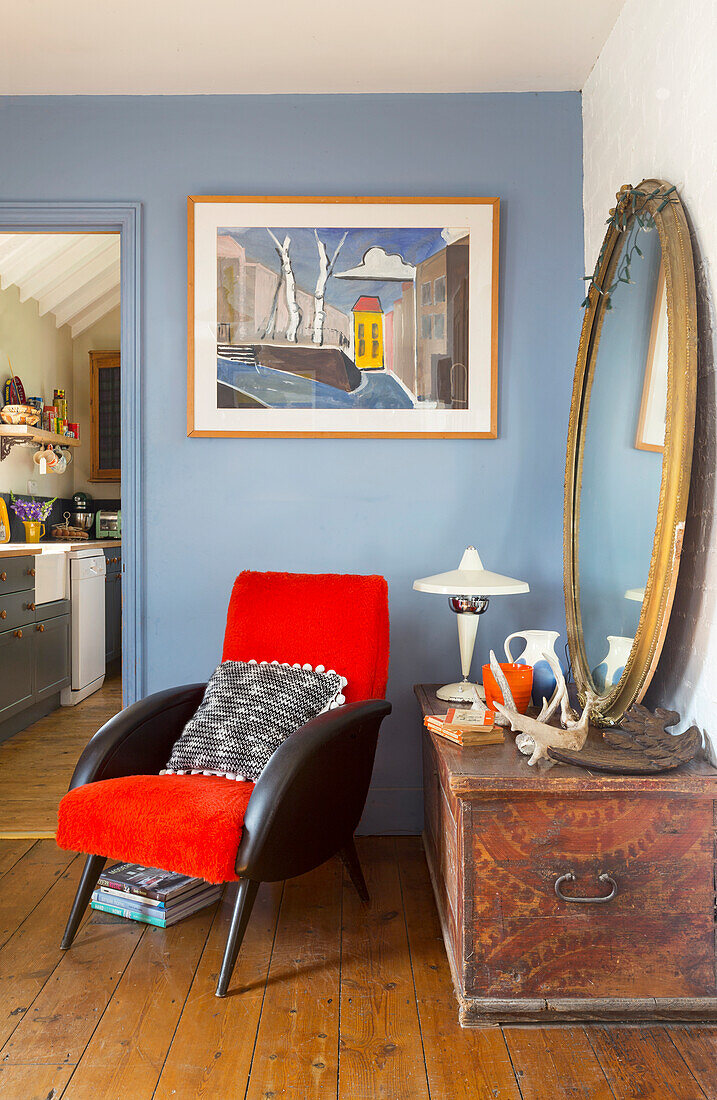 Living room with blue wall, red armchair, round mirror and antique chest
