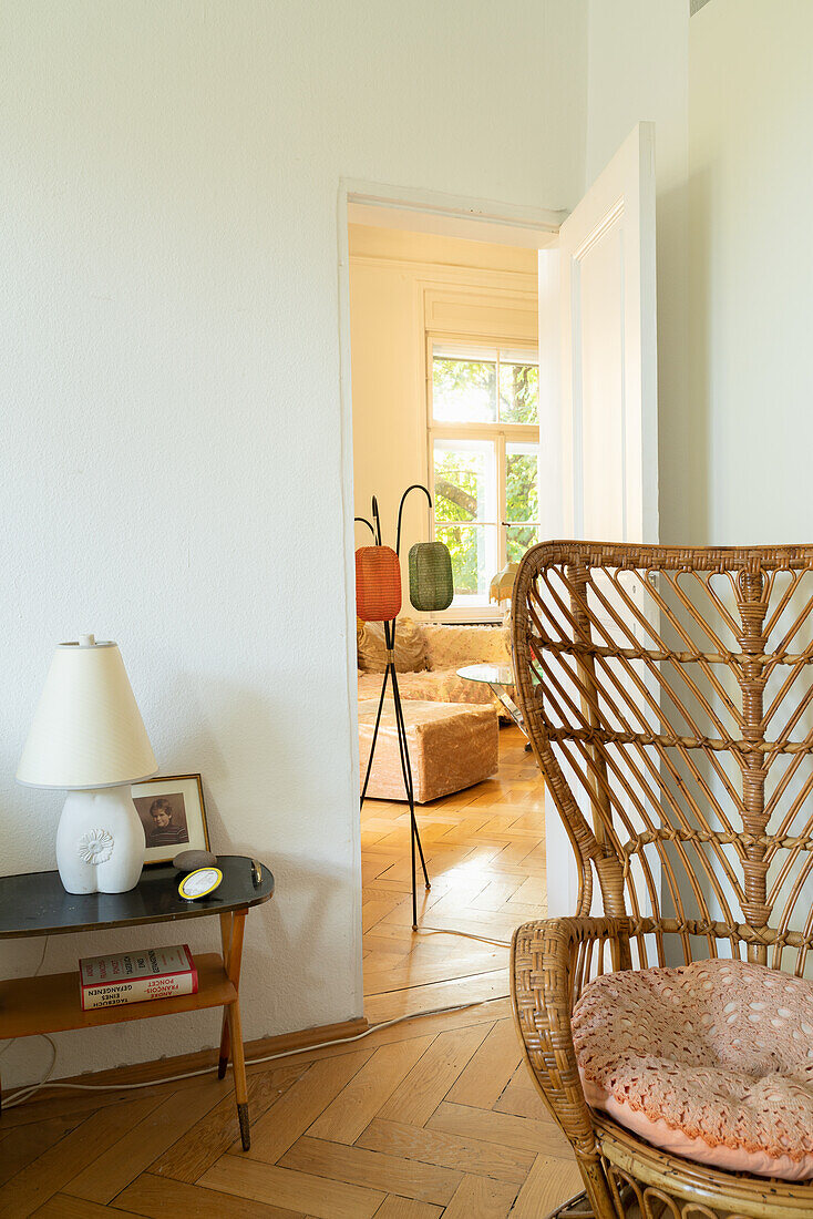 Mid-Century Beistelltisch und Vintage-Rattanstuhl in hellem Zimmer mit Fischgrätparkett, Blick ins Wohnzimmer