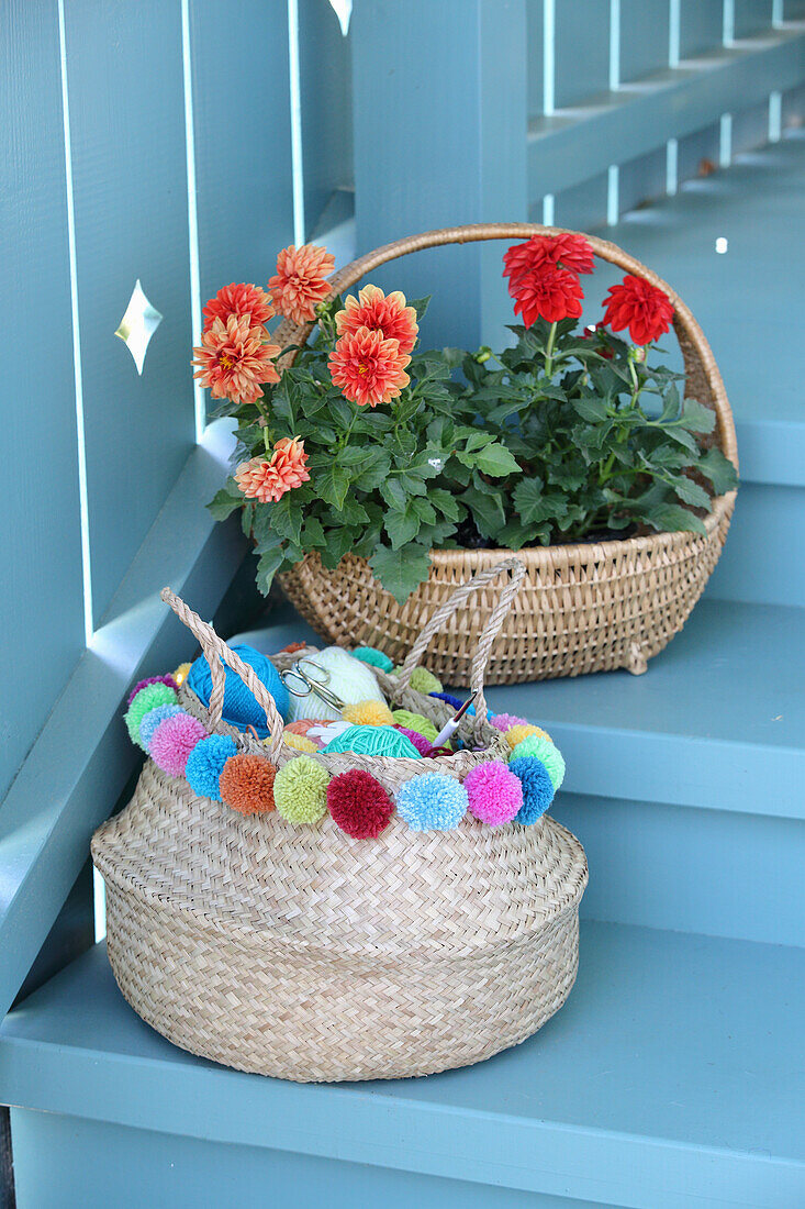 Knitting yarn in basket decorated with colourful pompoms and dahlias in wicker basket on steps