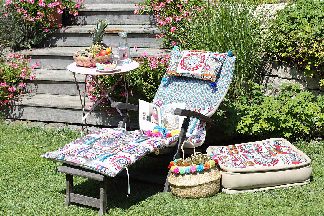 DIY-Liegenauflage, Bodenkissen mit Patchworkstoff und Korb mit bunten Pompons im Garten