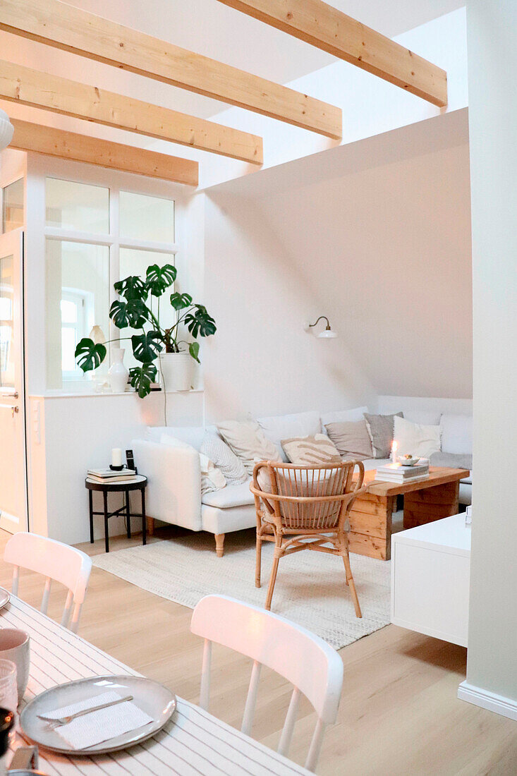 Living room with cream-coloured corner sofa, rattan armchairs and wooden beams on the ceiling