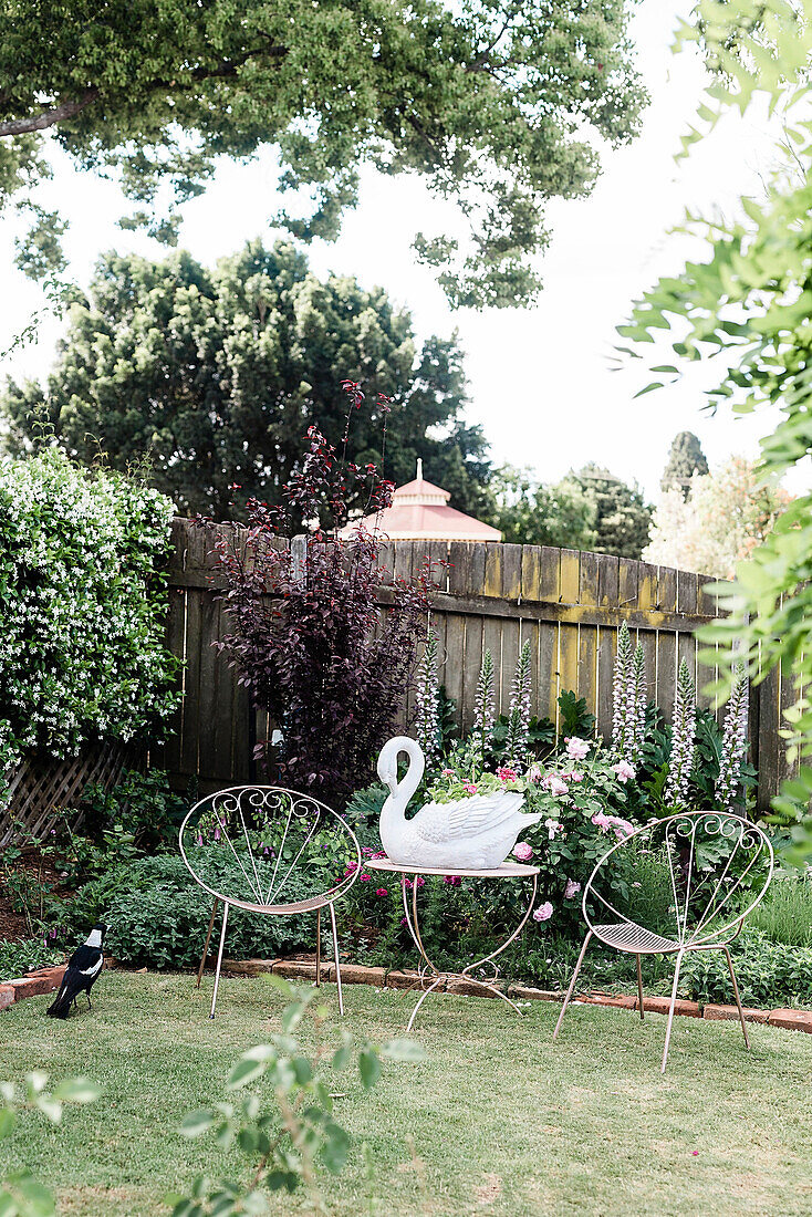 Filigrane Stühle und Tisch mit Schwanfigur im Garten