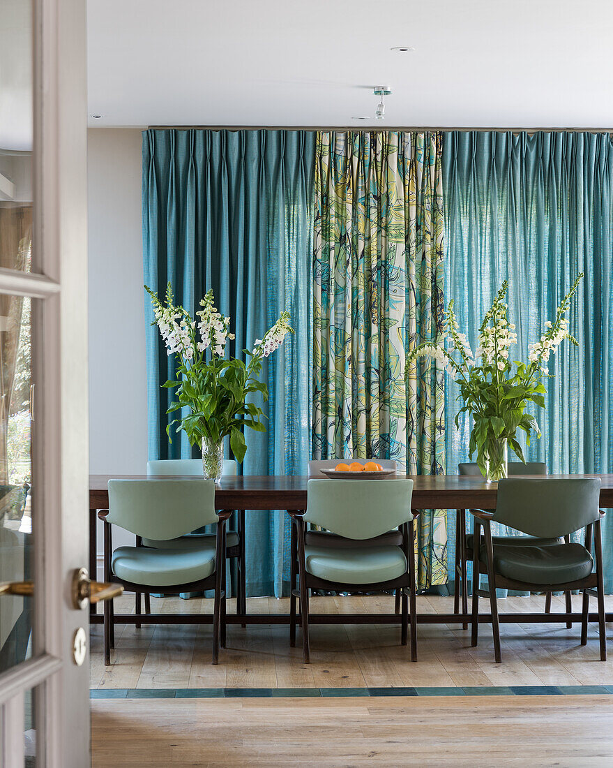 Esszimmer mit mintgrünen Stühlen, Blumenarrangements und gemusterten Gardinen