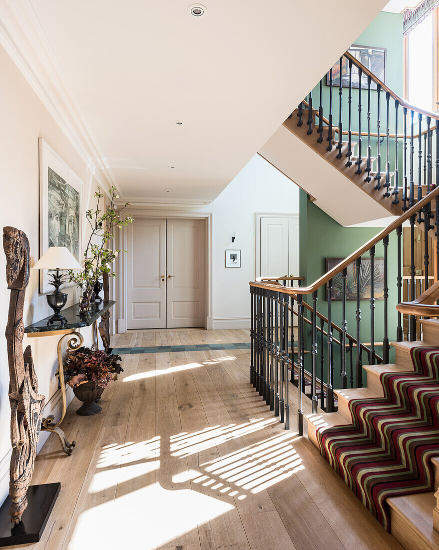 Hallway with wooden staircase, wrought-iron banister and striped runner