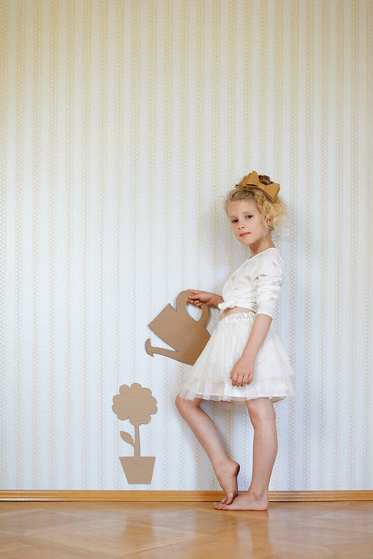 Porträt eines Mädchens, das mit einer Gießkanne aus Pappe und einer Blume spielt
