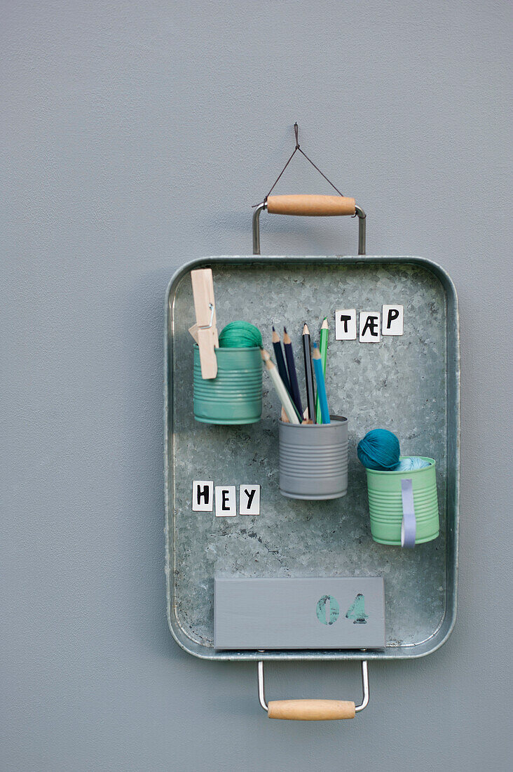 Office supplies in cans attached to metal tray hanging on wall