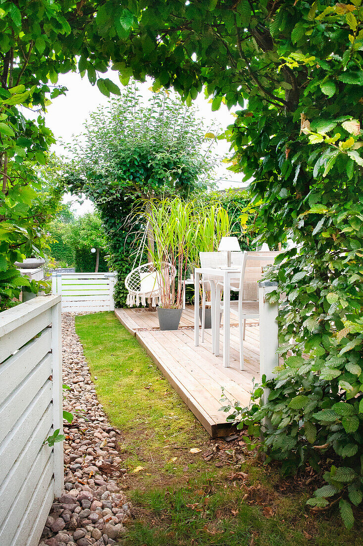 Holzterrasse mit Pflanzkübeln und Gartenmöbeln umgeben von Grün