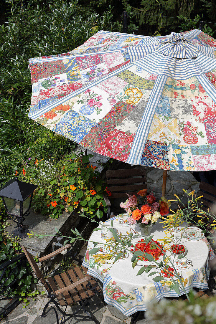 DIY-Sonnenschirm über Gartentisch mit Blumenstrauß und Erdbeerkuchen