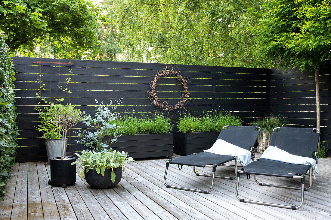 Sun deck with loungers and planter box, surrounded by black wooden privacy screens