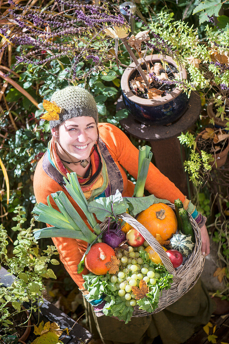 Lächelnde Frau mit Obst- und Gemüsekorb, während sie im Garten steht