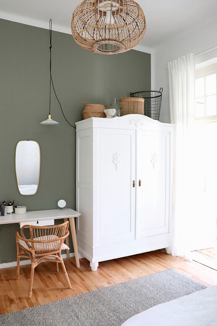 Bedroom with white wardrobe, rattan chair and green wall paint