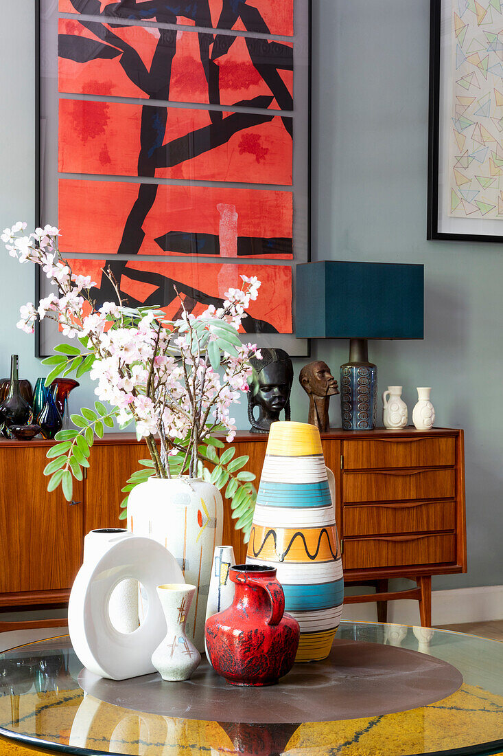 Vases on round coffee table in front of sideboard and modern artwork in living room