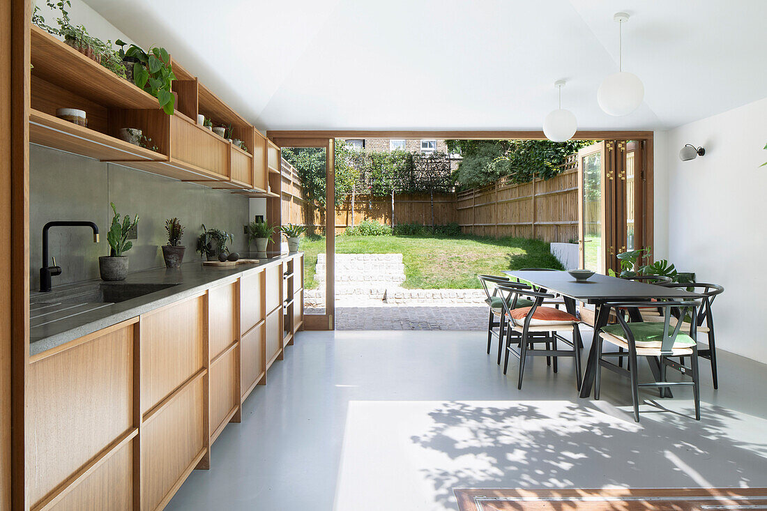 Maßgefertigte Küche mit Holzfronten und Essbereich, Blick in den sonnigen Garten