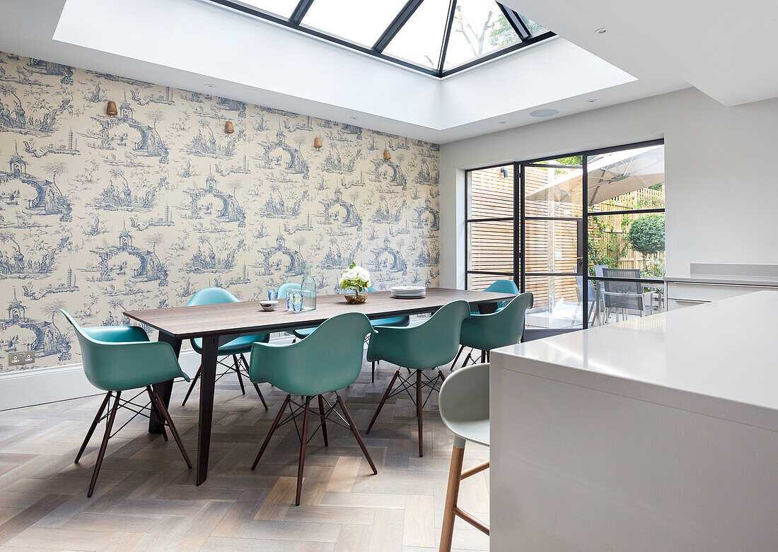 Dining area with turquoise-coloured chairs and wallpaper with Toile de Jouy pattern