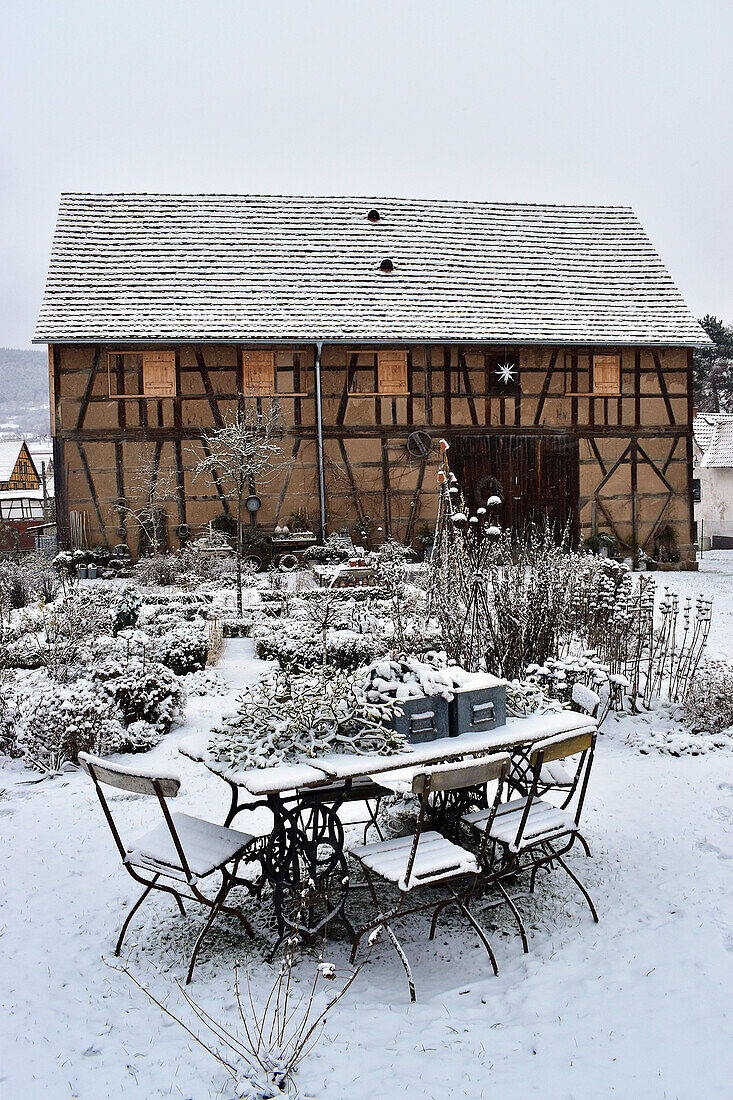 Snow-covered cottage garden in front of barn