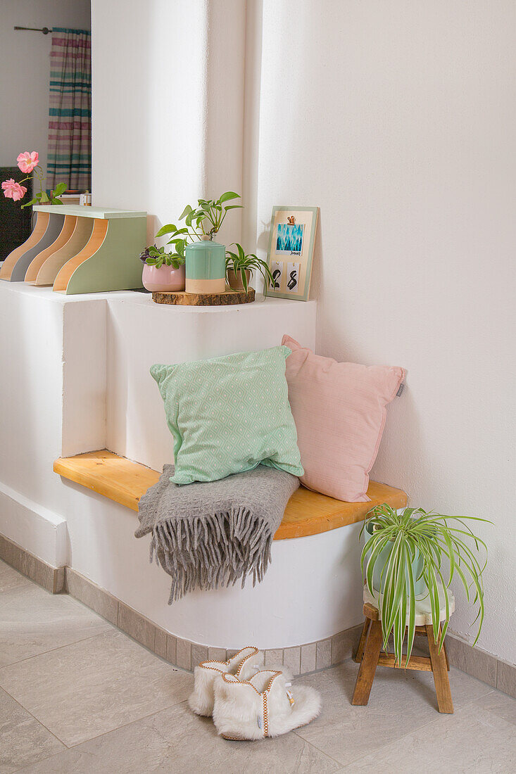 Small seating area with cushions and blanket, houseplant on stool